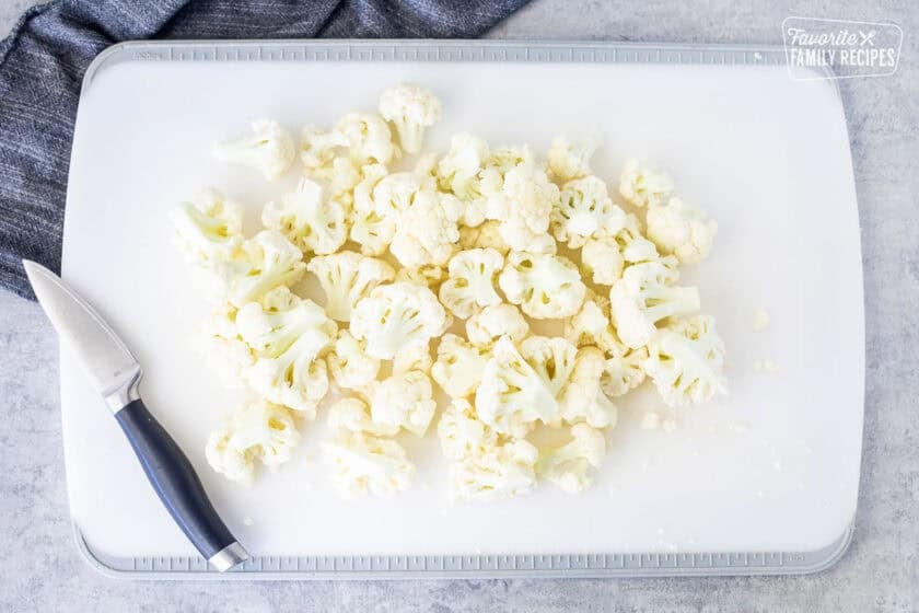 Cut up pieces of cauliflower on a cutting board with a knife.