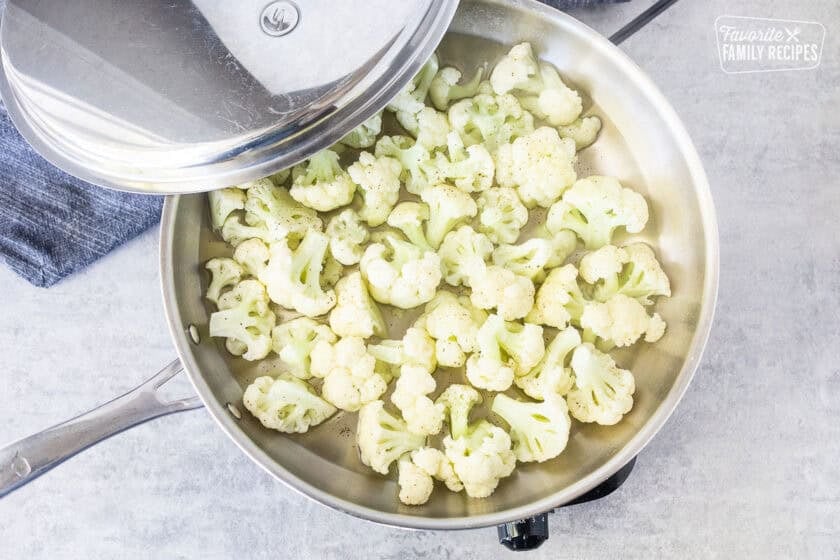 Steamed cauliflower in a skillet with lid.