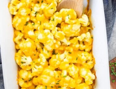 Baking dish with Cheesy Cauliflower Side Dish and wooden spoon.
