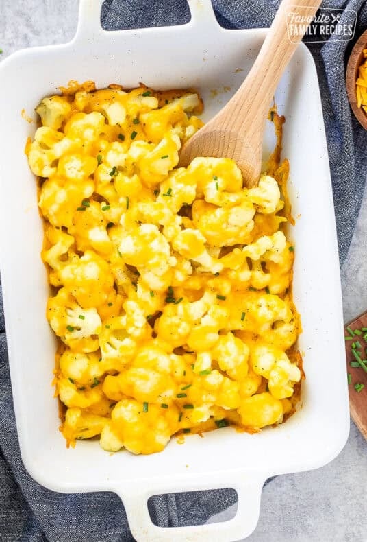 Baking dish with Cheesy Cauliflower Side Dish and wooden spoon.