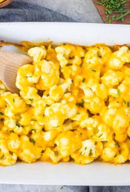 Baking dish with Cheesy Cauliflower Side Dish and wooden spoon.
