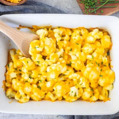 Baking dish with Cheesy Cauliflower Side Dish and wooden spoon.