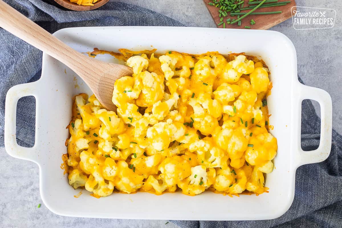 Baking dish with Cheesy Cauliflower Side Dish and wooden spoon.