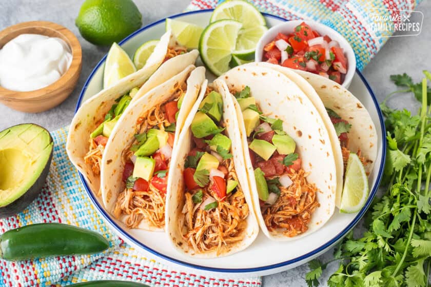 Crockpot chicken tacos on a plate garnished with pico de Gallo, avocado and cilantro.