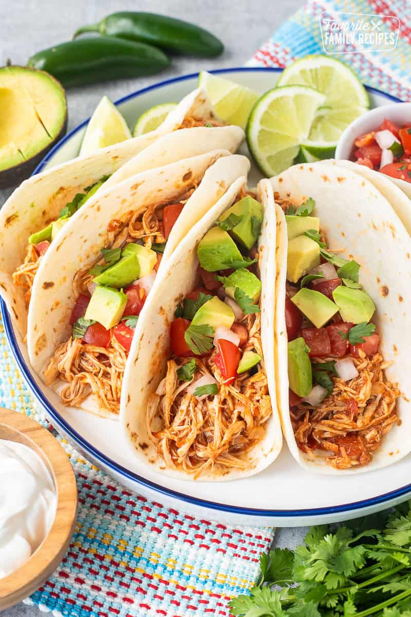 Crockpot chicken tacos on a plate garnished with pico de Gallo, avocado and cilantro.