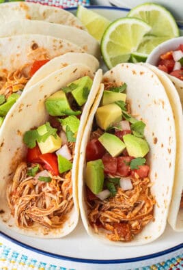 Crockpot chicken tacos on a plate garnished with pico de Gallo, avocado and cilantro.