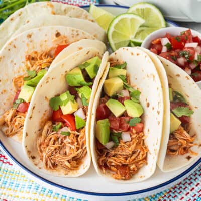 Crockpot chicken tacos on a plate garnished with pico de Gallo, avocado and cilantro.