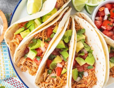 Crockpot chicken tacos on a plate garnished with pico de Gallo, avocado and cilantro.