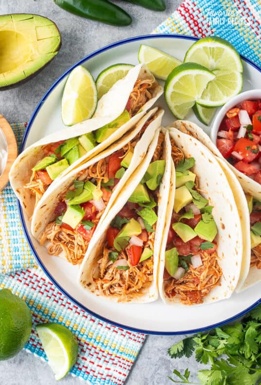 Crockpot chicken tacos on a plate garnished with pico de Gallo, avocado and cilantro.