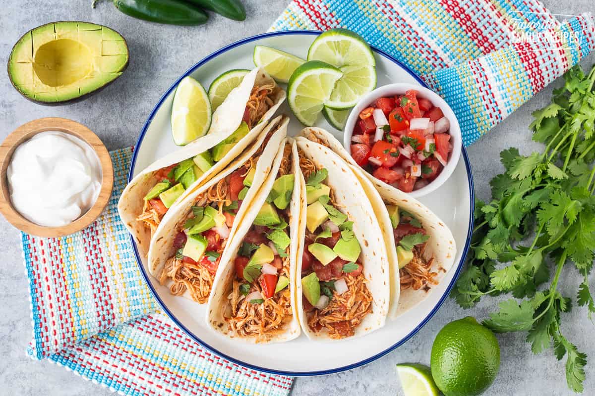 Crockpot chicken tacos on a plate garnished with pico de Gallo, avocado and cilantro.