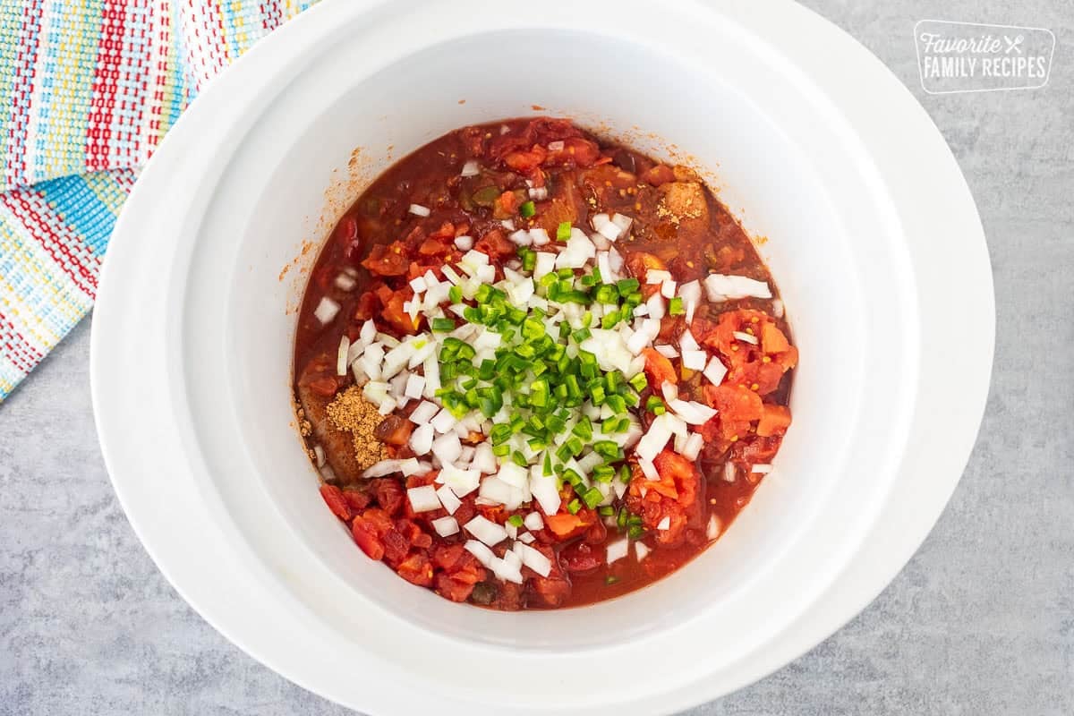 Crockpot with chicken breast, taco seasoning, tomatoes, onion and jalapeño.