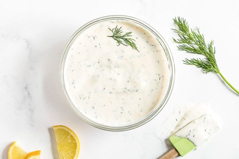 Lemon dill dip for dipping fried green beans in a clear bowl garnished with fresh dill