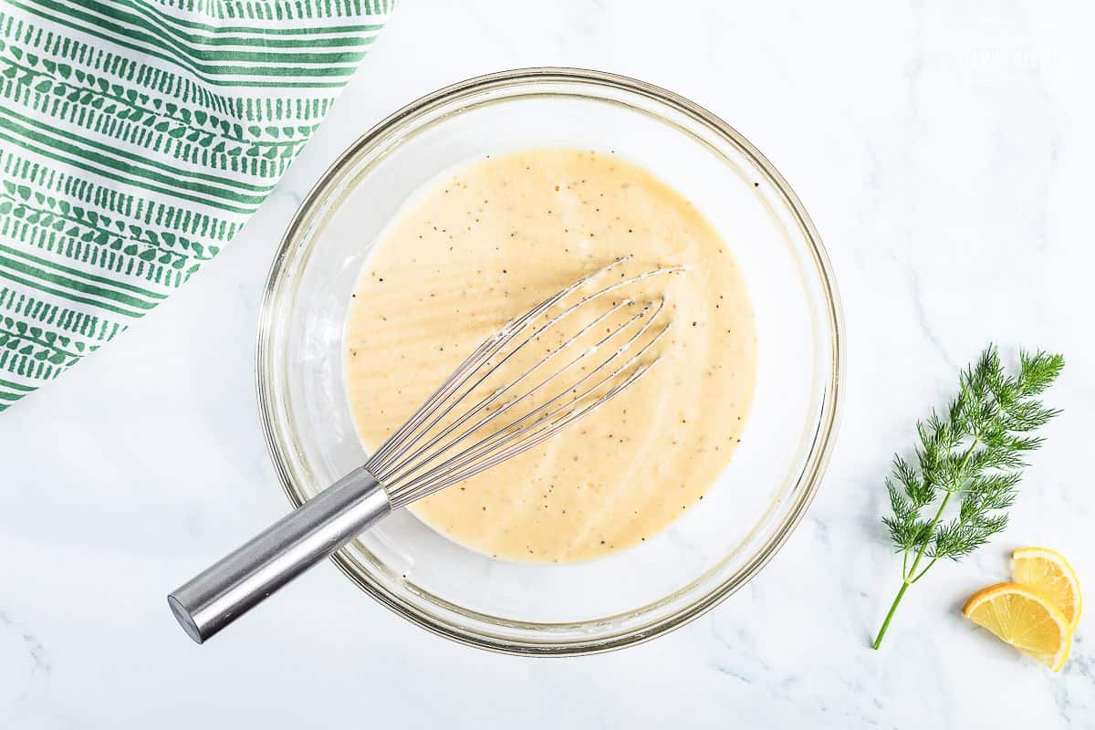 Batter to dip fried green beans in a bowl with a whisk on a white counter top
