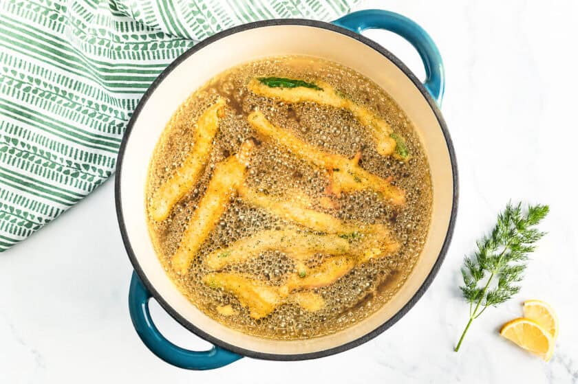 Green beans frying in a Dutch oven with the oil hot and bubbling around the golden green beans