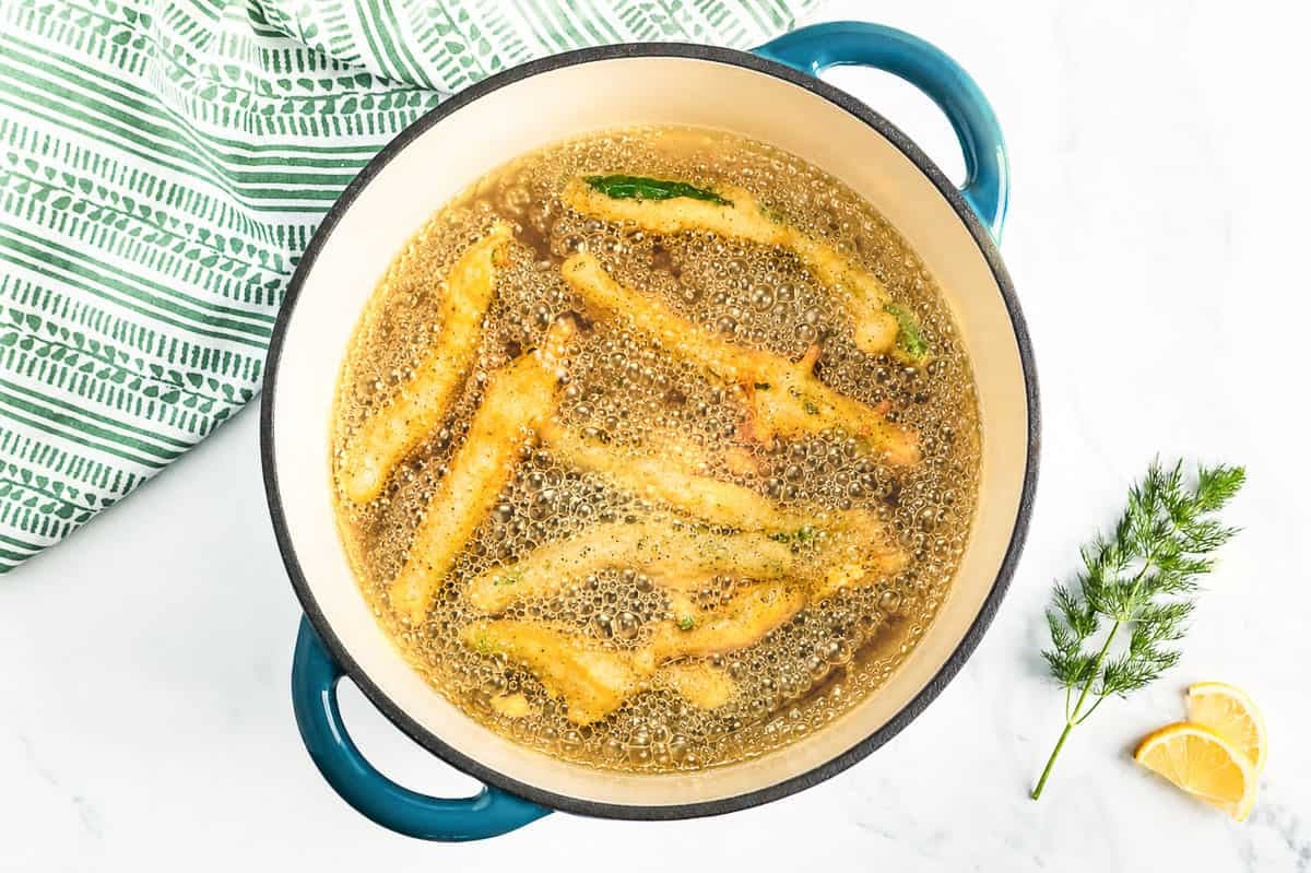 Green beans frying in a Dutch oven with the oil hot and bubbling around the golden green beans