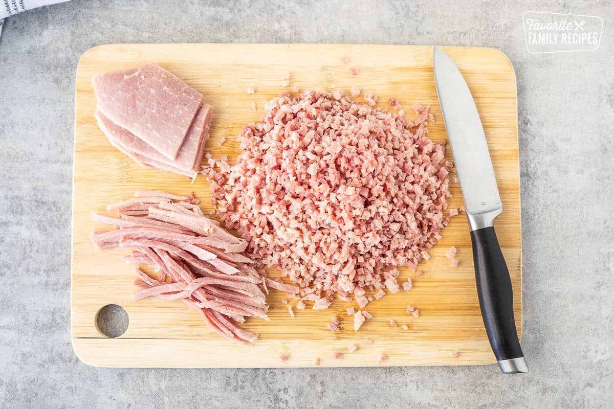 Cutting board with chipped up ham pieces and a knife.