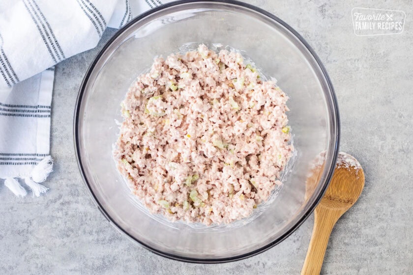 Mixing bowl with ham salad and wooden spoon on the side.