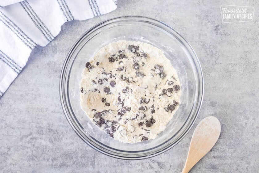 Glass mixing bowl with dry ingredients combined with wooden spoon.