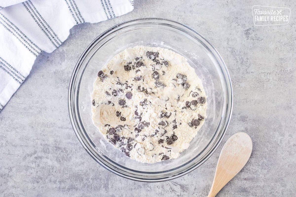 Glass mixing bowl with dry ingredients combined with wooden spoon.