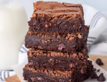 Stacked homemade brownies with a glass of milk.