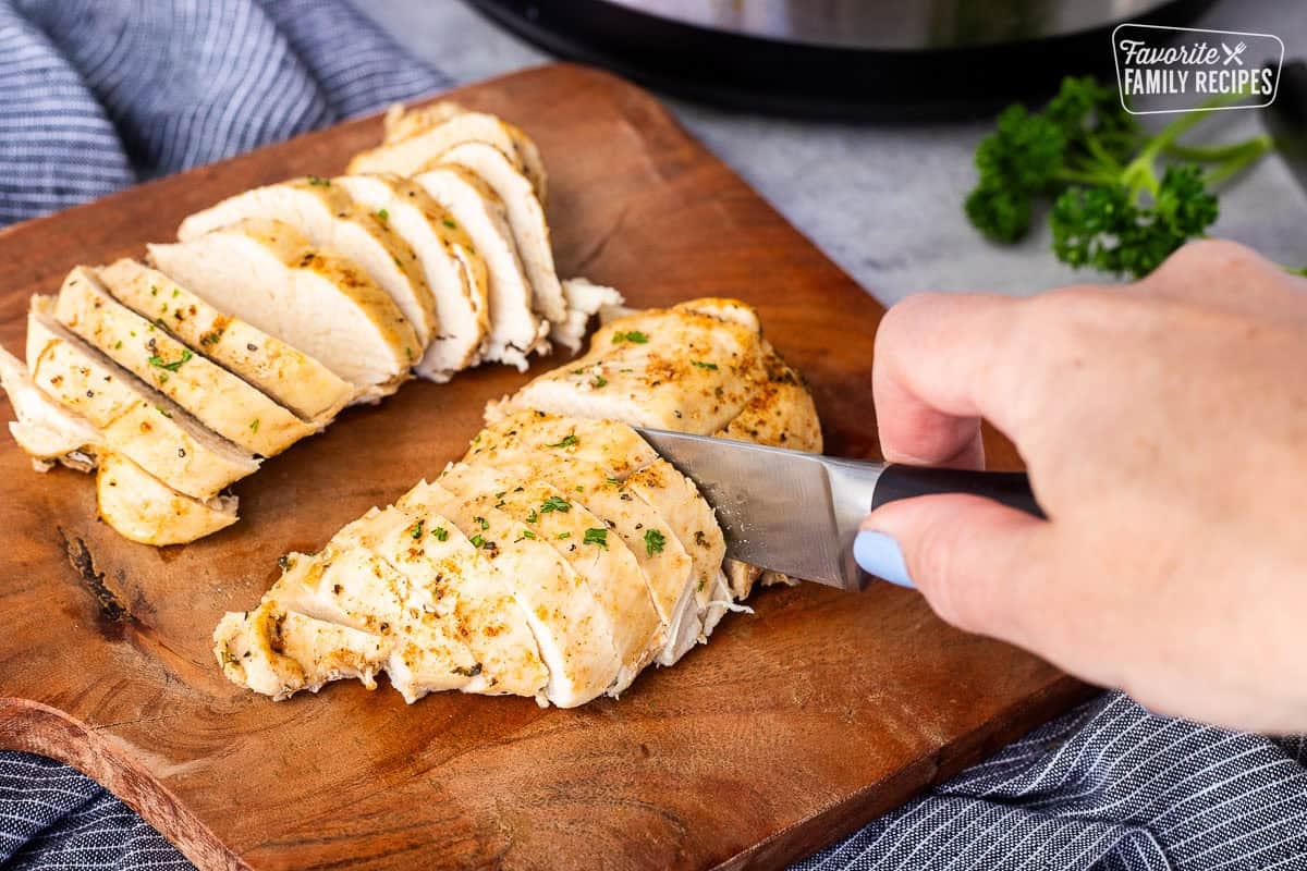 Cutting cooked seasoned chicken breasts on a cutting board with a knife.