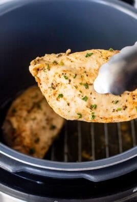 Tongs holding a seasoned chicken breast out of the instant pot.