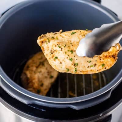 Tongs holding a seasoned chicken breast out of the instant pot.