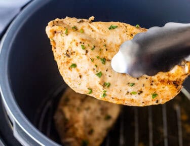 Tongs holding a seasoned chicken breast out of the instant pot.