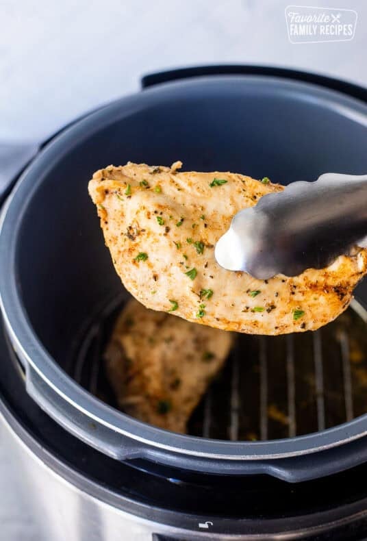 Tongs holding a seasoned chicken breast out of the instant pot.