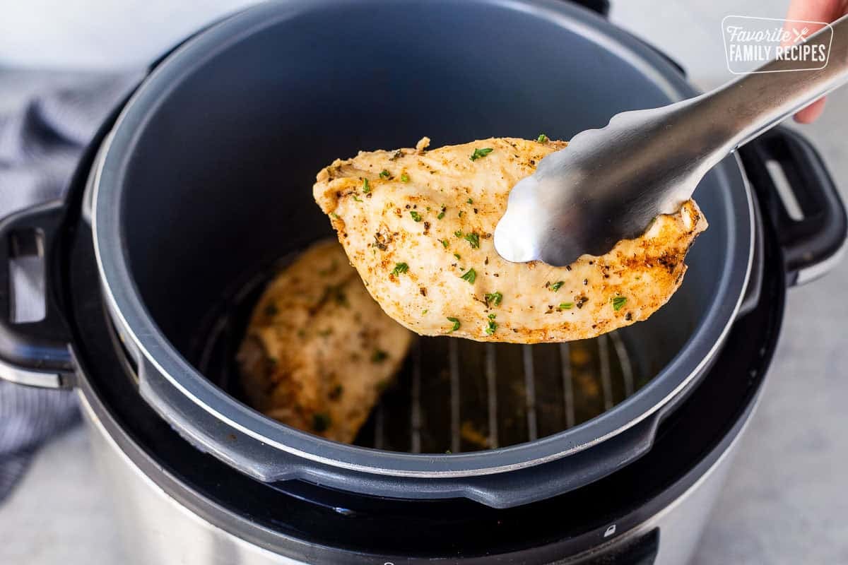 Tongs holding a seasoned chicken breast out of the instant pot.