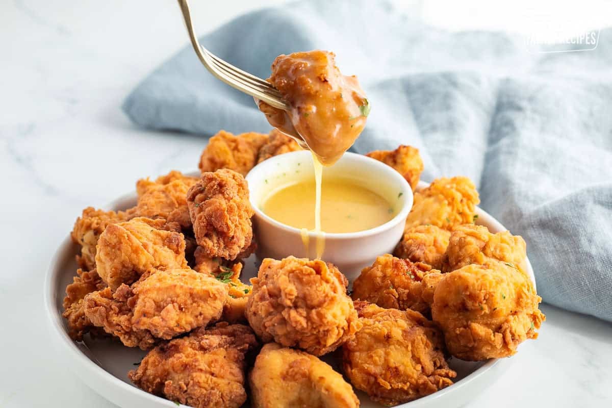 Dipping a piece of Mafa Chicken with a fork into honey mustard sauce.