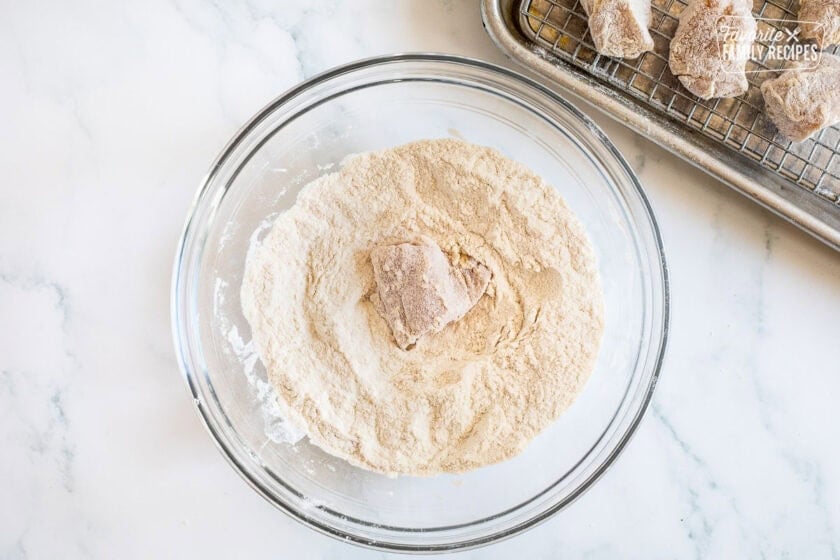 Chicken piece covered with Wondra flour in a large glass bowl.