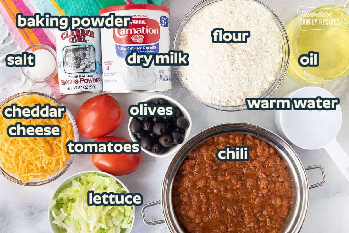 Ingredients to make Navajo Tacos including salt, baking powder, dry milk, flour, oil, water, chili, olives, tomatoes, cheese and lettuce.