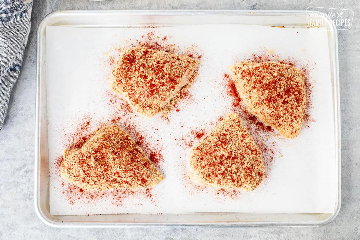 Paprika sprinkled on unbaked chicken on a sheet pan.