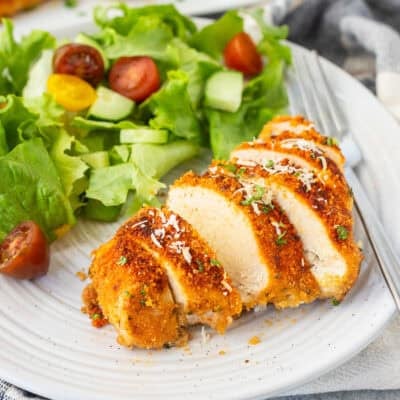 Parmesan chicken cut on a plate with a side of salad.