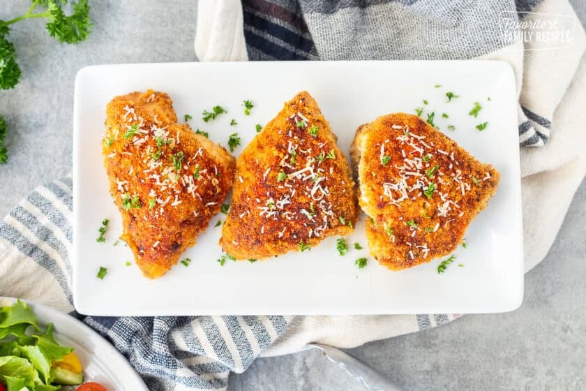 Baked parmesan chicken on a plate and garnished with parsley and fresh parmesan cheese.
