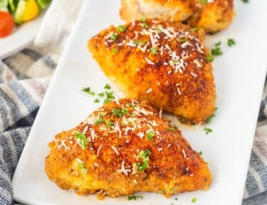 Baked parmesan chicken on a plate and garnished with parsley and fresh parmesan cheese.