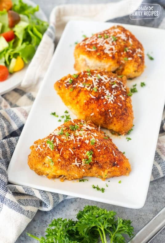 Baked parmesan chicken on a plate and garnished with parsley and fresh parmesan cheese.