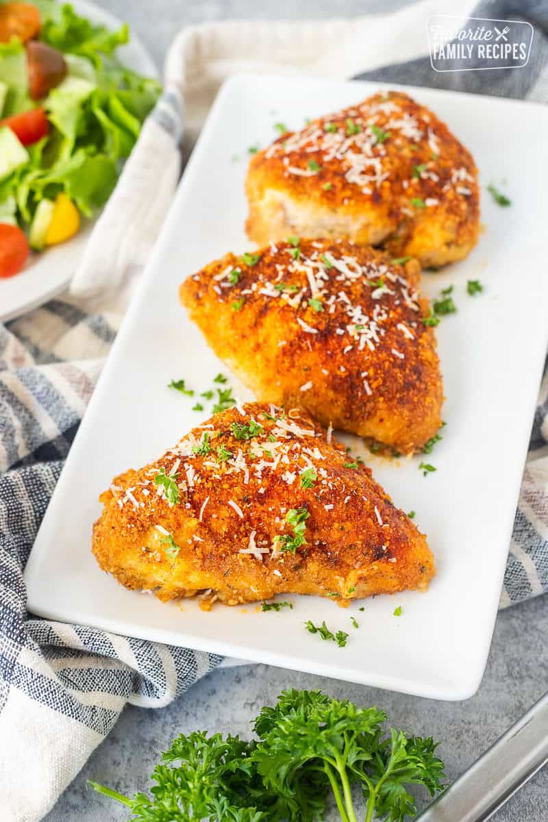 Baked parmesan chicken on a plate and garnished with parsley and fresh parmesan cheese.