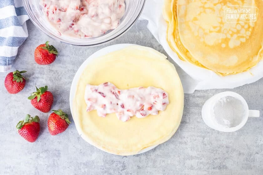 Crepe with strawberry cream cheese filling next to strawberry filling and crepes.