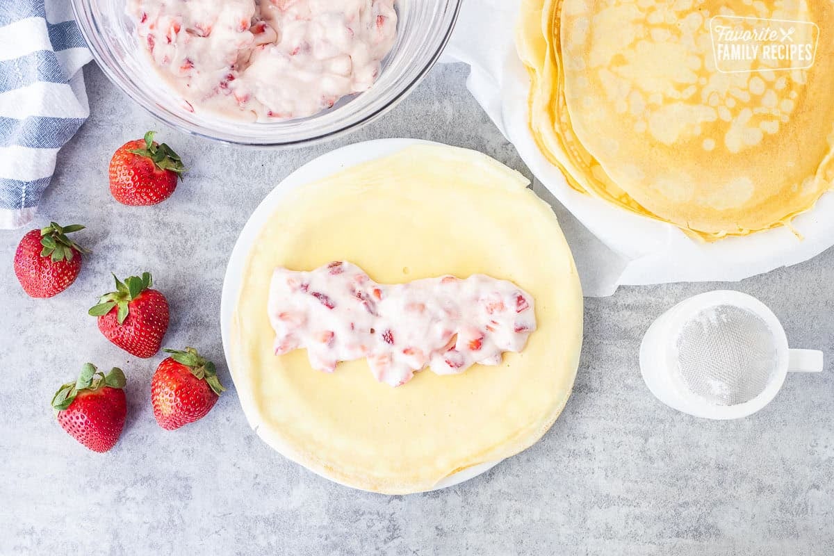 Crepe with strawberry cream cheese filling next to strawberry filling and crepes.