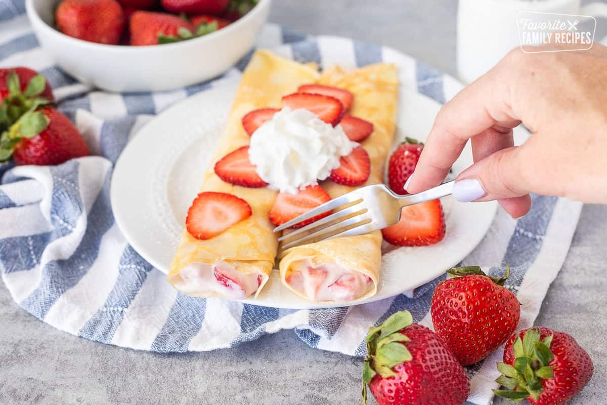 Cutting strawberry crepe with a fork on a plate.