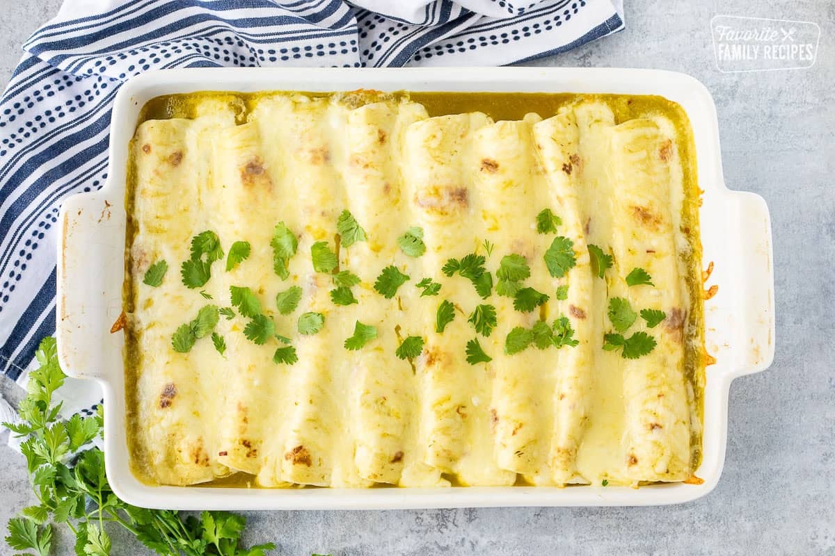White baking dish with sweet pork enchiladas with melted cheese over the top and topped with cilantro.