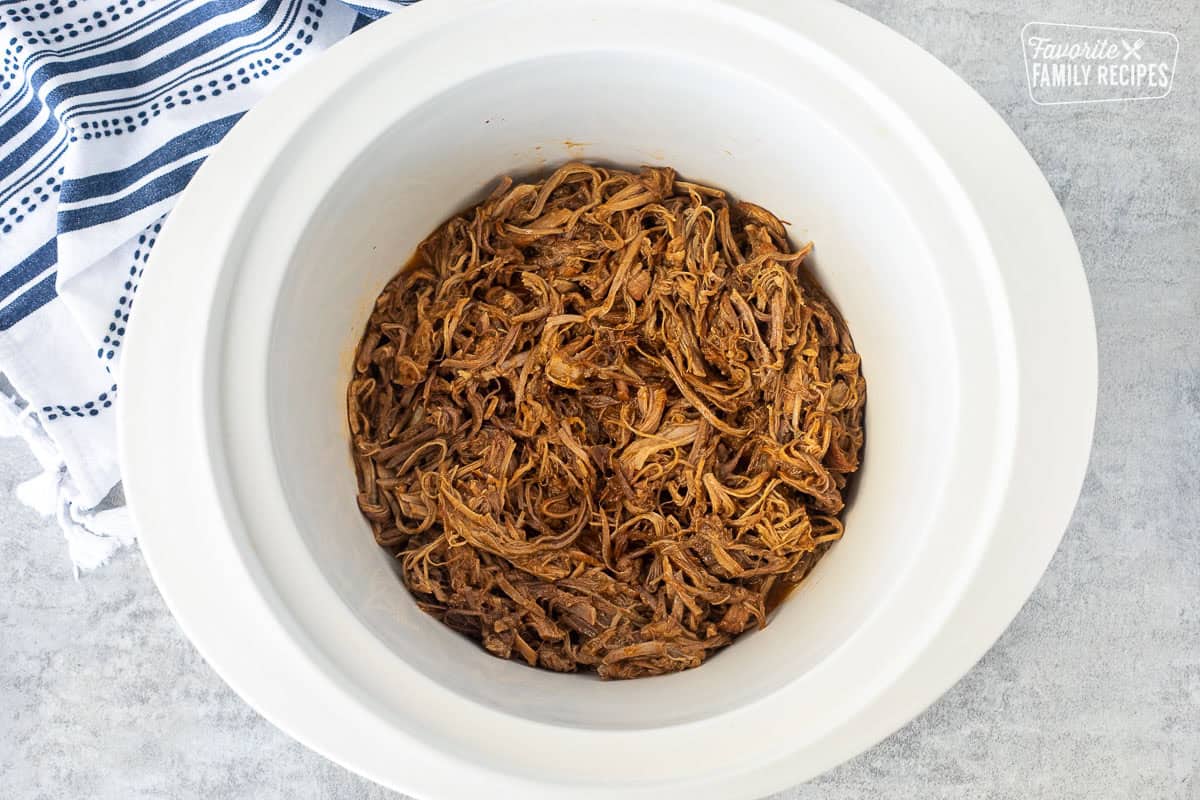 Tender shredded sweet pulled pork in a white Crockpot showing the tender juiciness of the pork.