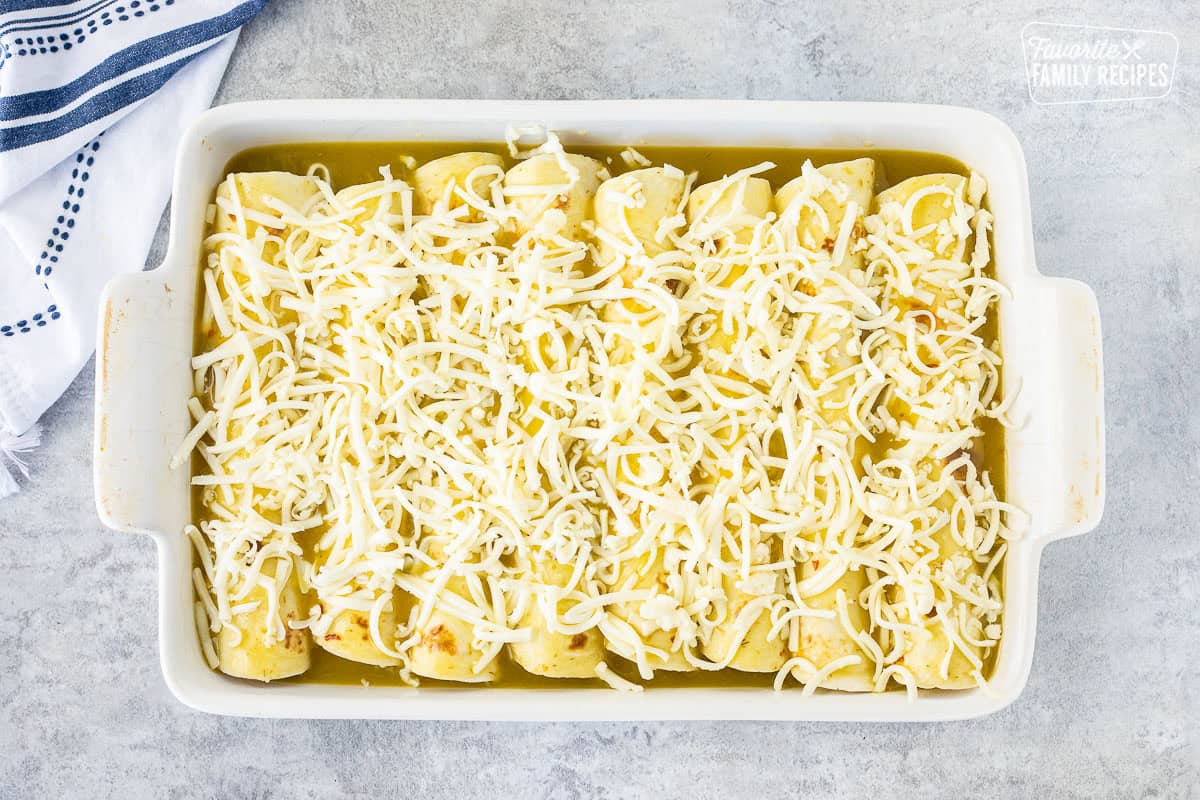 Rolled sweet pork enchiladas unbaked in a pan with green enchilada sauce and shredded Monterey Jack cheese.