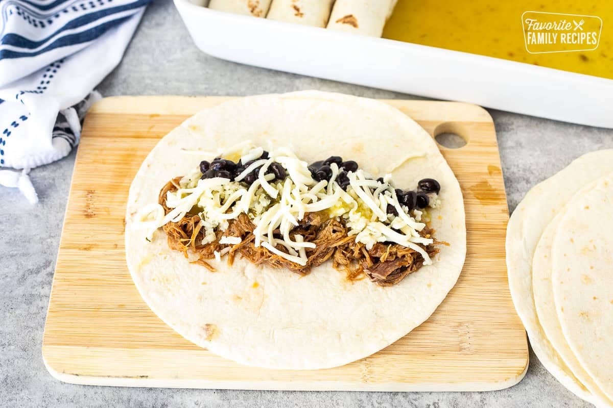 Sweet pulled pork, black beans, rice, green sauce and cheese on a tortilla before being rolled into an enchilada.