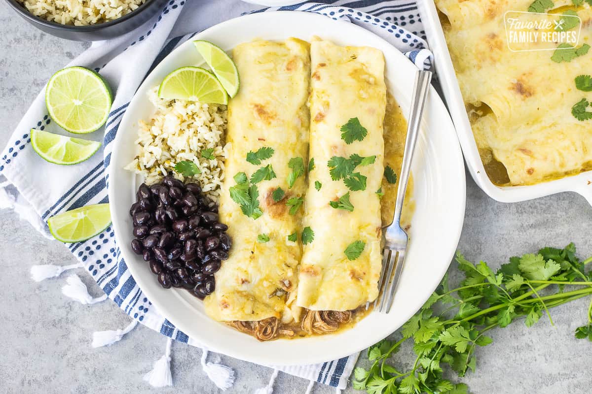 Two sweet pork enchiladas with green enchilada sauce on a white plate with cilantro lime rice and black beans on the side.