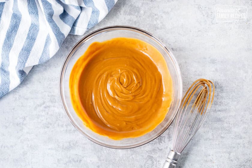 Glass bowl with peanut sauce and whisk on the side.