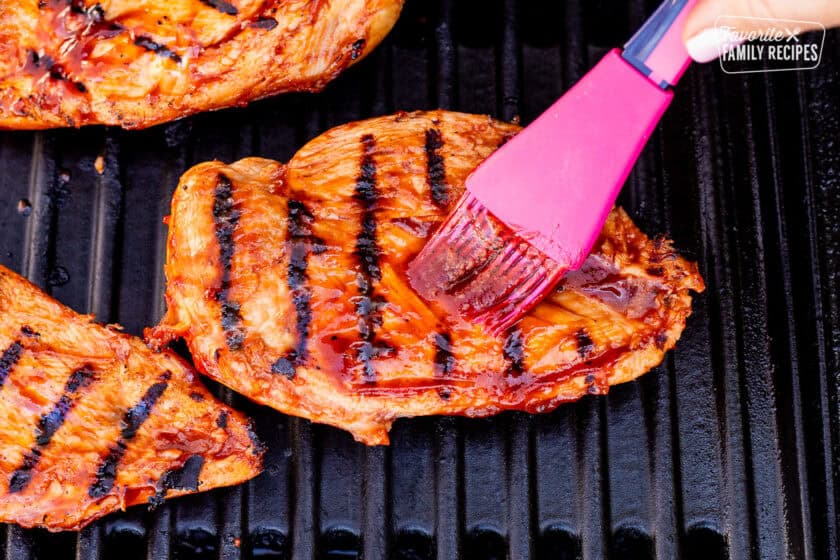 Brushing BBQ sauce onto chicken breast on the barbecue.