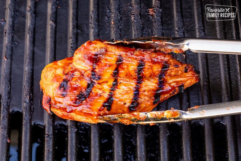 Removing barbecue chicken breast from the grill with tongs.